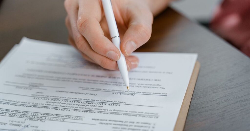 A hand signing a document with a pen.