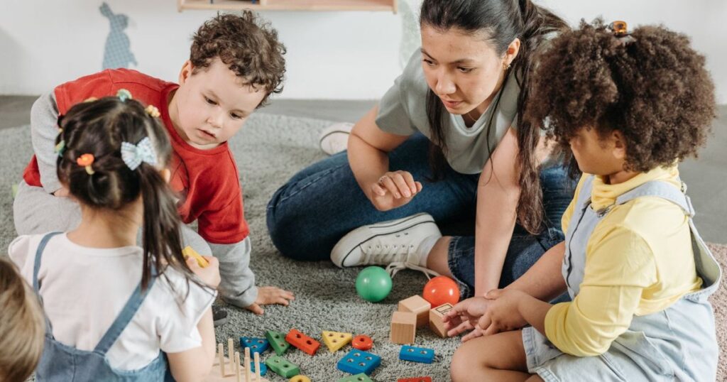 Kids and a teacher playing with toys in a colorful kindergarten classroom.