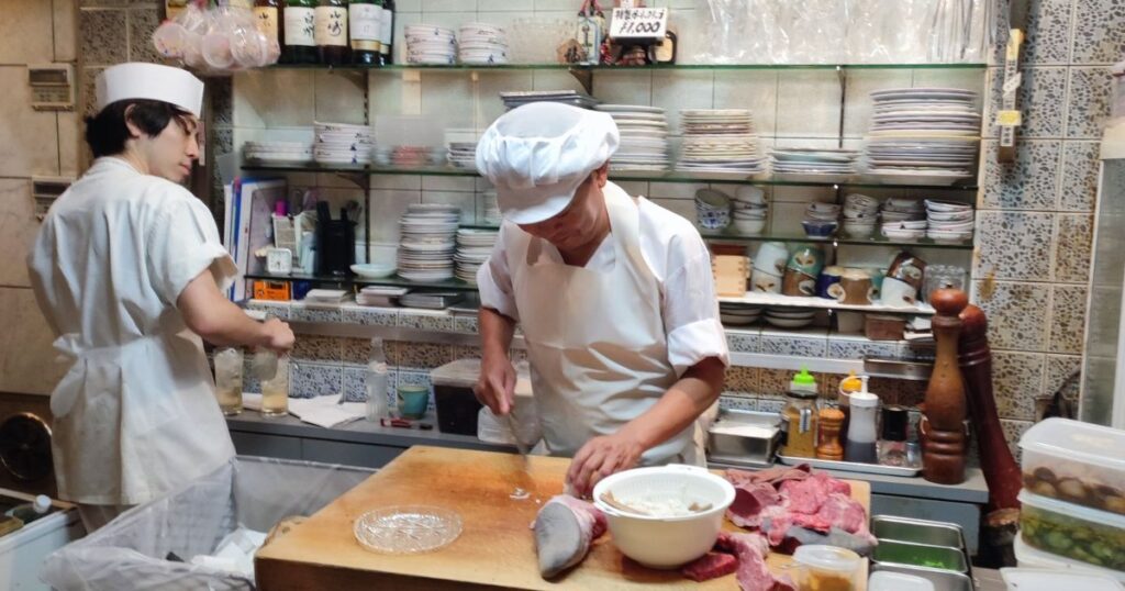 Two chefs preparing food in a busy restaurant kitchen.