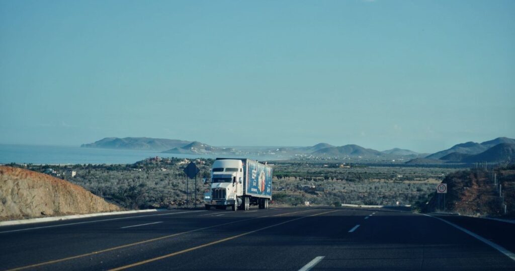 A semi-truck driving on a highway with mountains in the background.