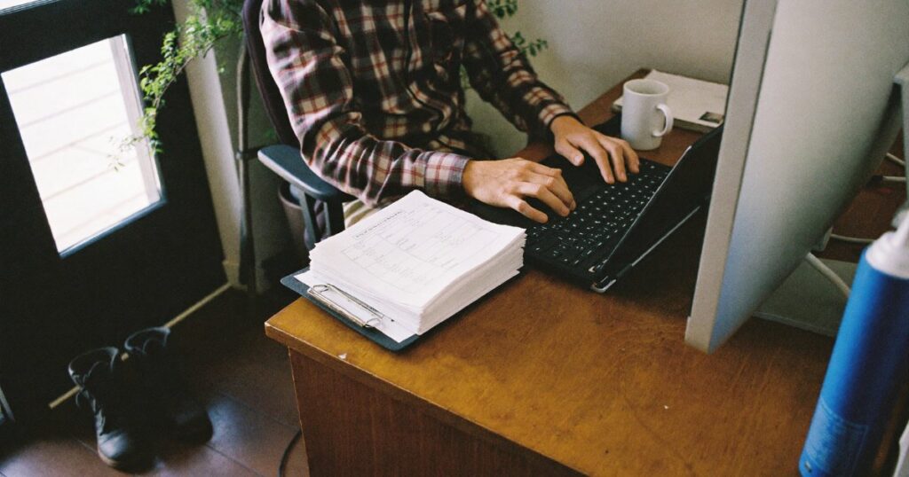 Small business owner running payroll on a laptop with timesheets on the desk