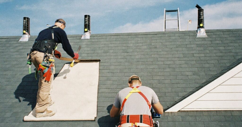 Roofers in safety harnesses installing shingles on a house roof
